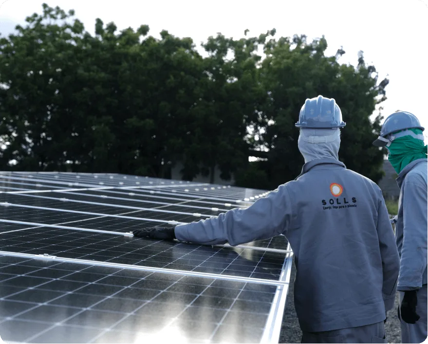 Dois técnicos da Solls com equipamento de proteção ao lado de painéis solares em solo